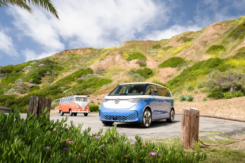 2025 VW ID. Buzz and vintage VW Bus parked in front of rolling hills.