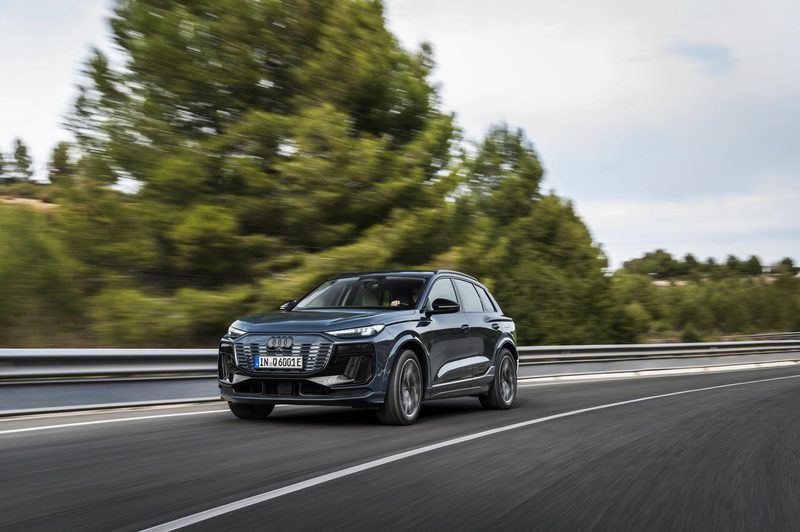 Audi Q6 e-tron driving on a highway with trees, land, and ocean in the background.