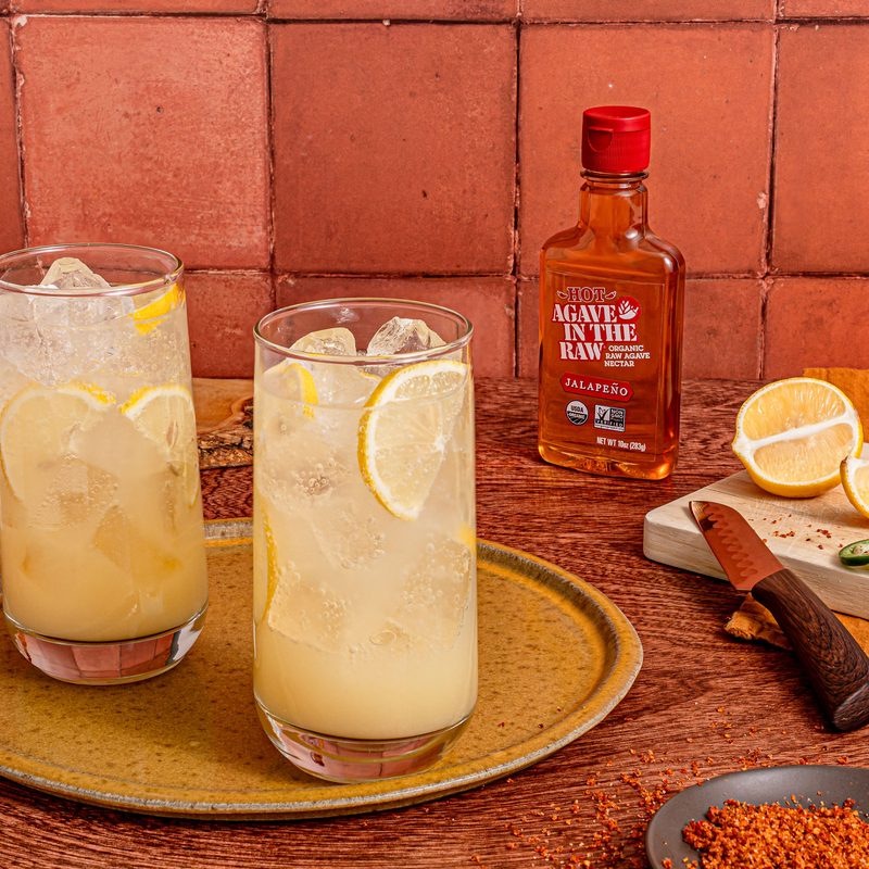 Two glasses of Spicy Lemonade Spriz cocktail with bottle of organic hot agave in the raw