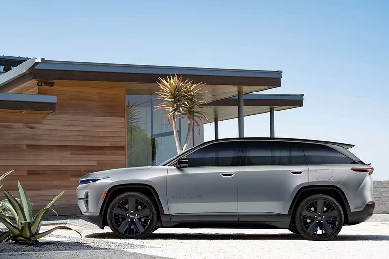 Jeep Wagoneer S all-electric model left profile parjed on sand beside a beach house.