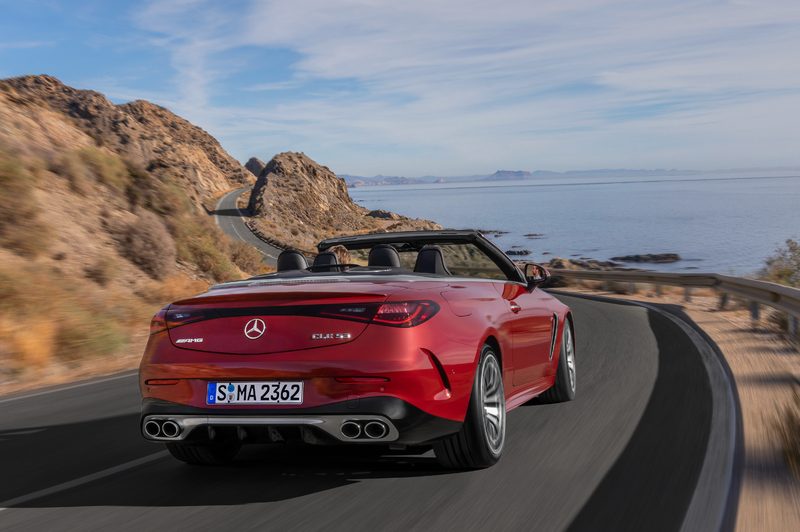 Mercedes-AMG CLE 53 Cabriolet rear view red with top down driving on a curved shore route between ocean and hills.
