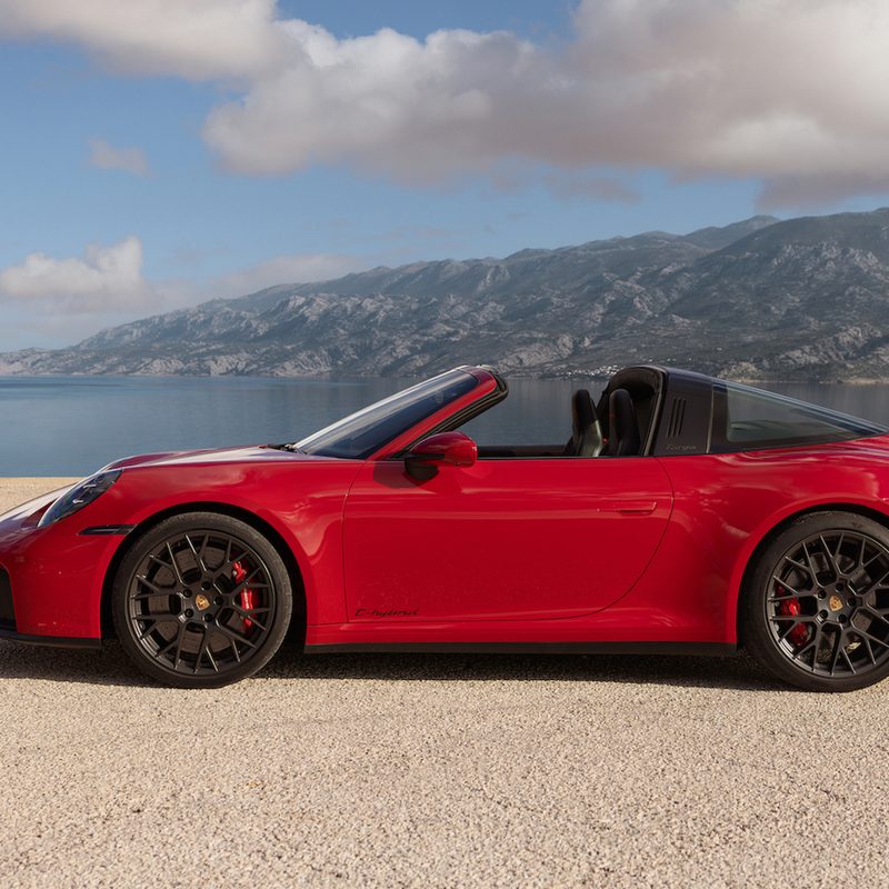 Porsche 911 Targa hybrid left profile parked on sand with a lake and mountain in the background.
