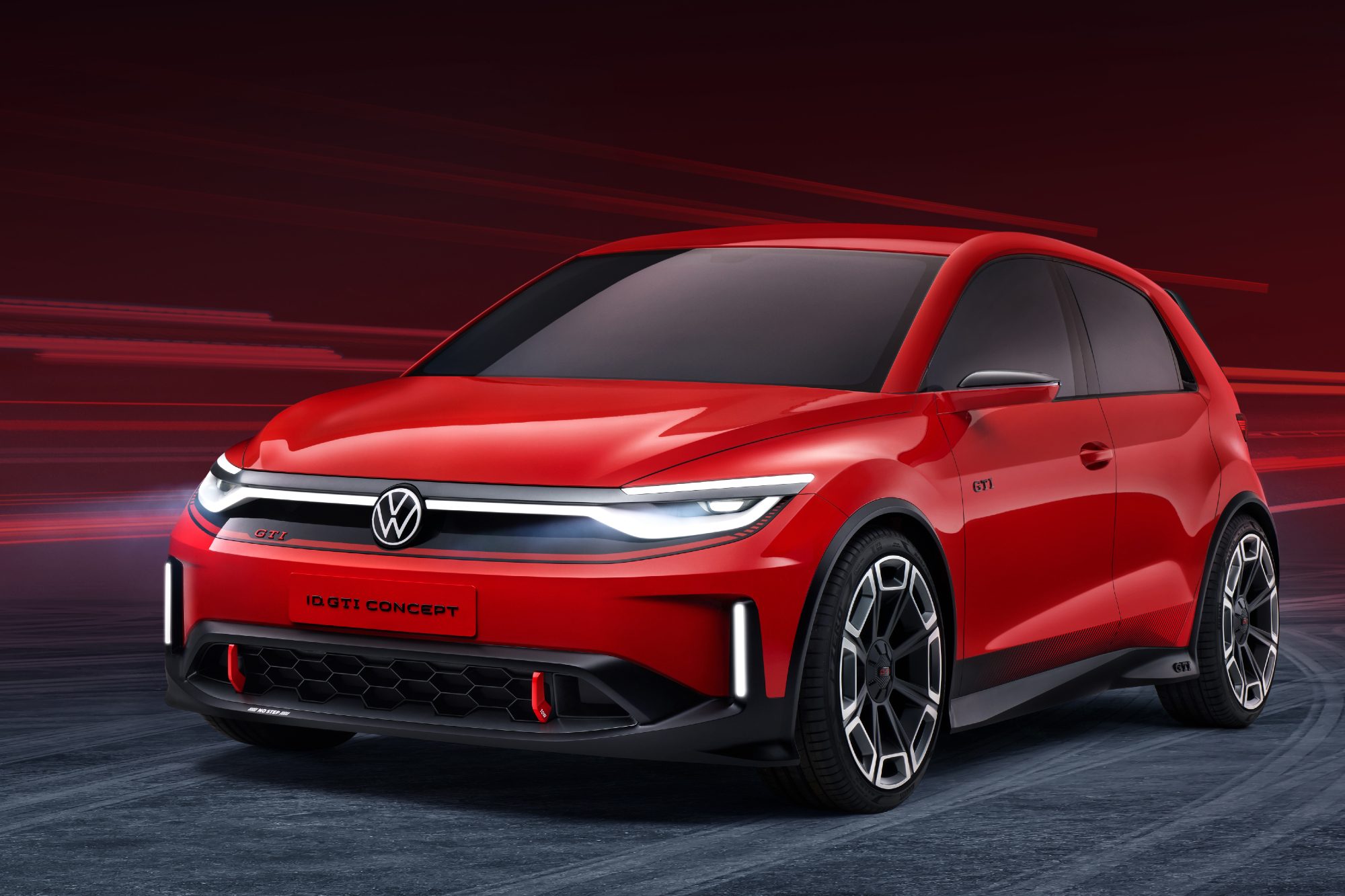 Volkswagen GTI EV concept in red left front three-quarter view on a loose gray gravel surface.