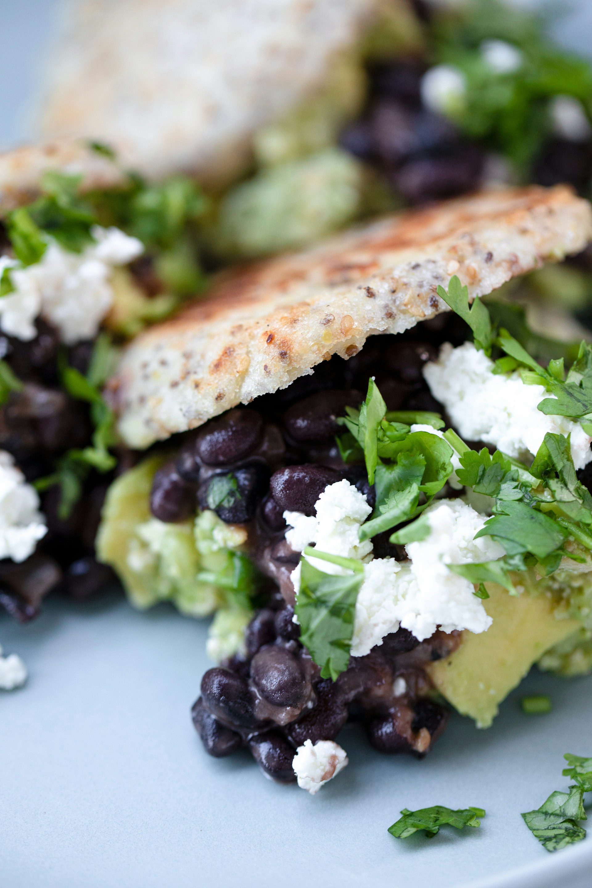 black beans with goat cheese and lettuce in sandwich close up on blue table