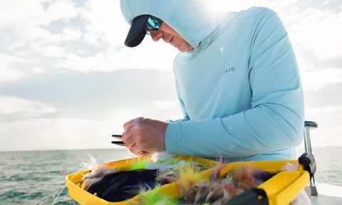 Man fishing on a boat while wearing an Orvis DriCast sun protection hoodie.