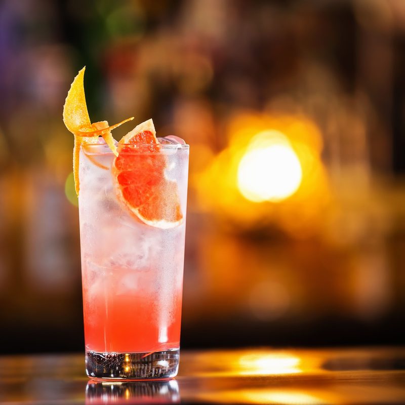 Closeup glass of greyhound cocktail decorated with grapefruit at bright bar counter background.