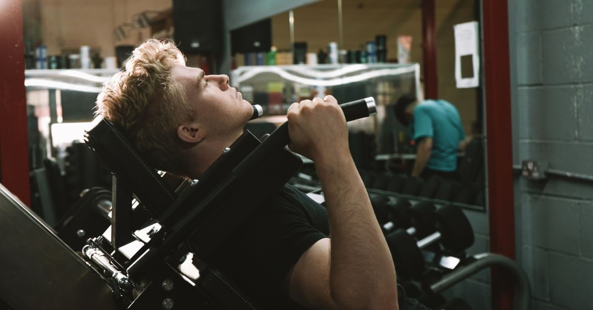 blonde-haired man doing a hack squat on a hack squat machine