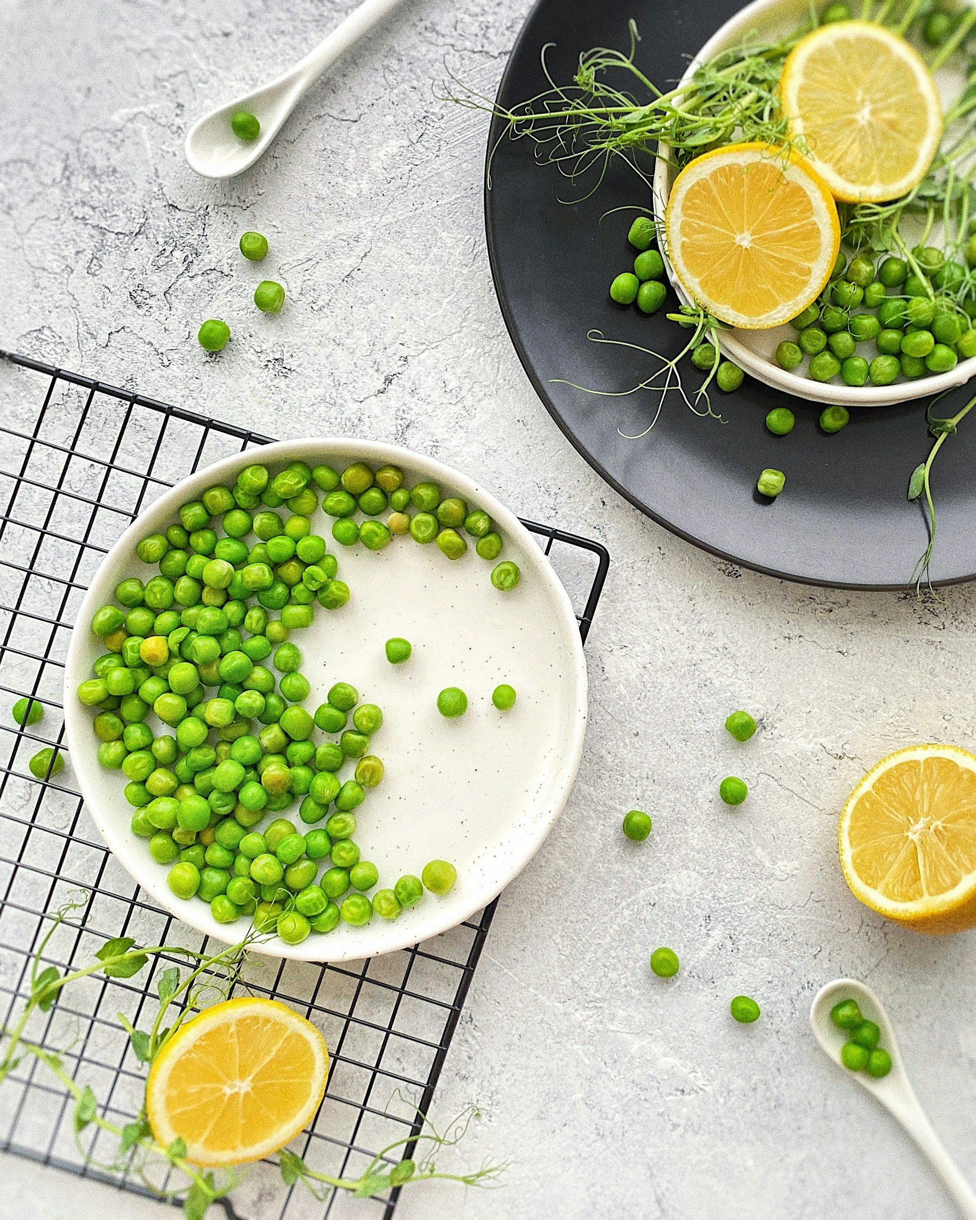 green peas in white bowl then another white bowl with lemon on white table