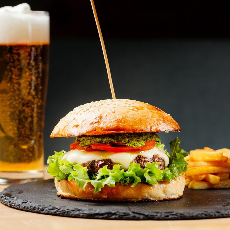 Beef burger with tomatos and fries on black plate with pint of lager beer on background.
