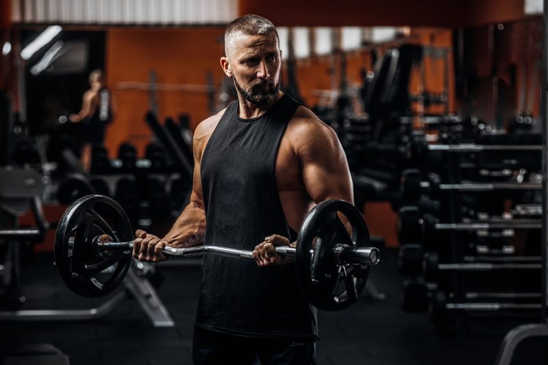 Fit strong man doing biceps curl with barbell in gym