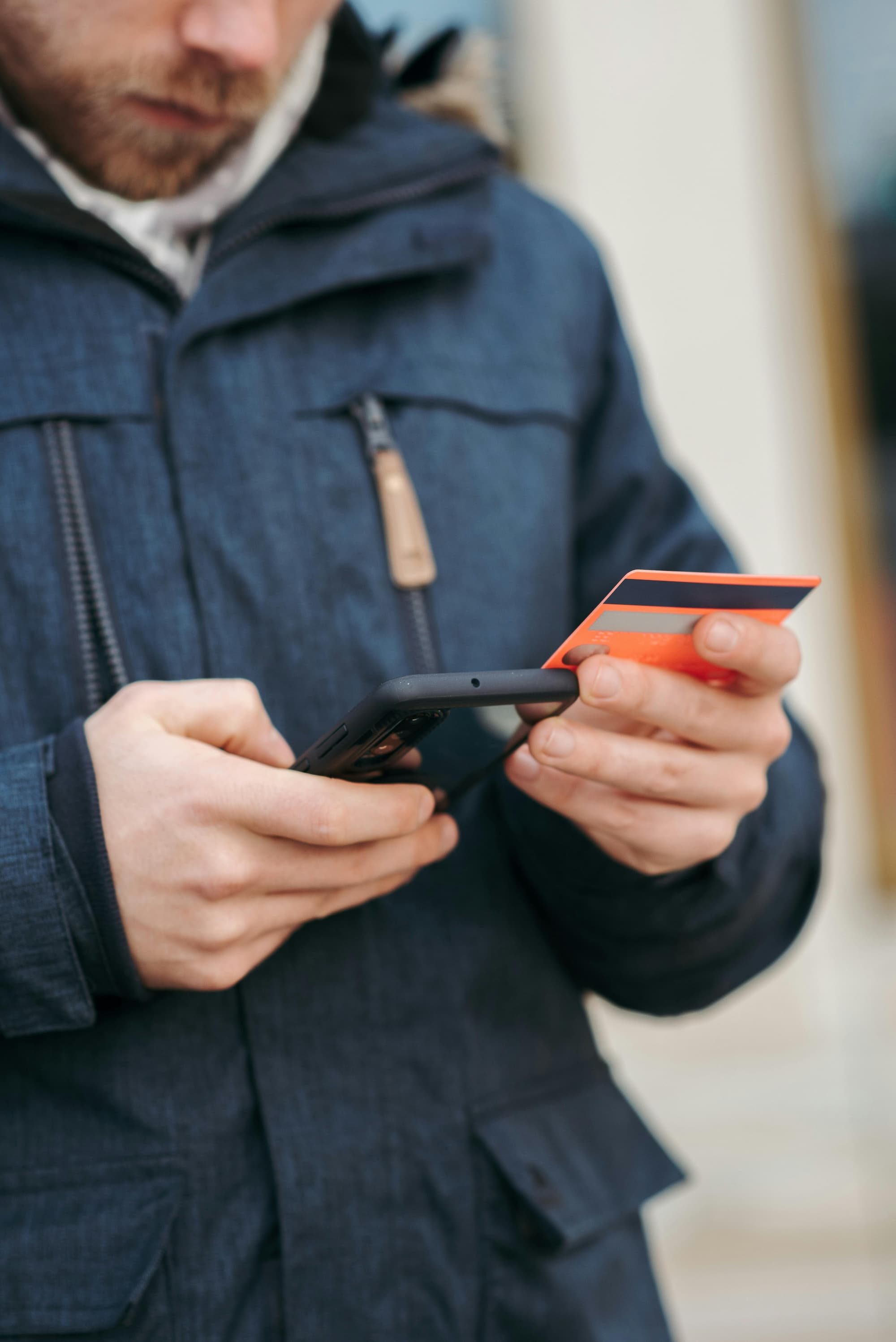 man looking at phone and credit card outside