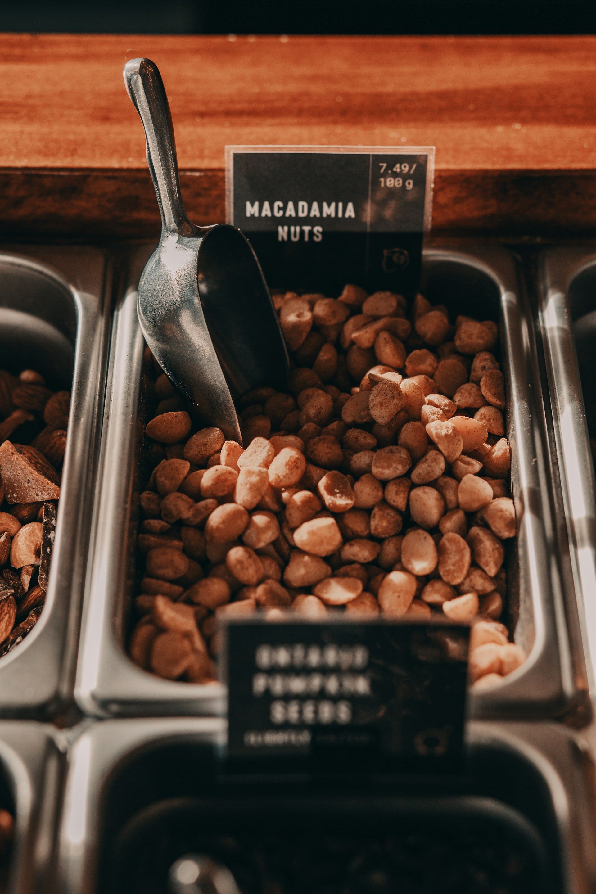 macadamia nuts in a grey trey with a scoop labeled by wooden counter