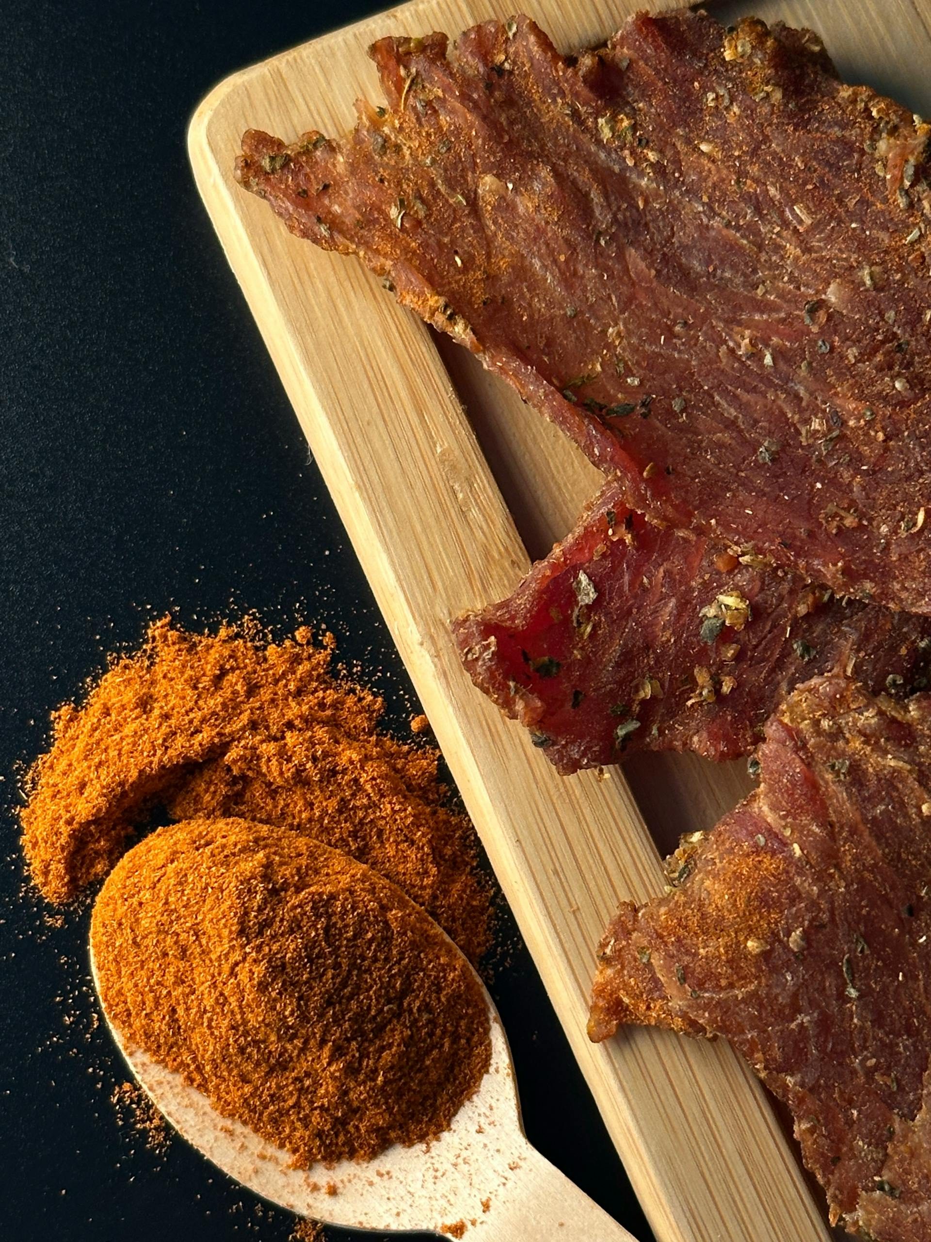 beef jerky with seasoning herb on wooden cutting board with black background