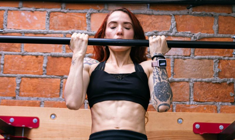 woman doing chin up wearing gym clothes near a brick wall