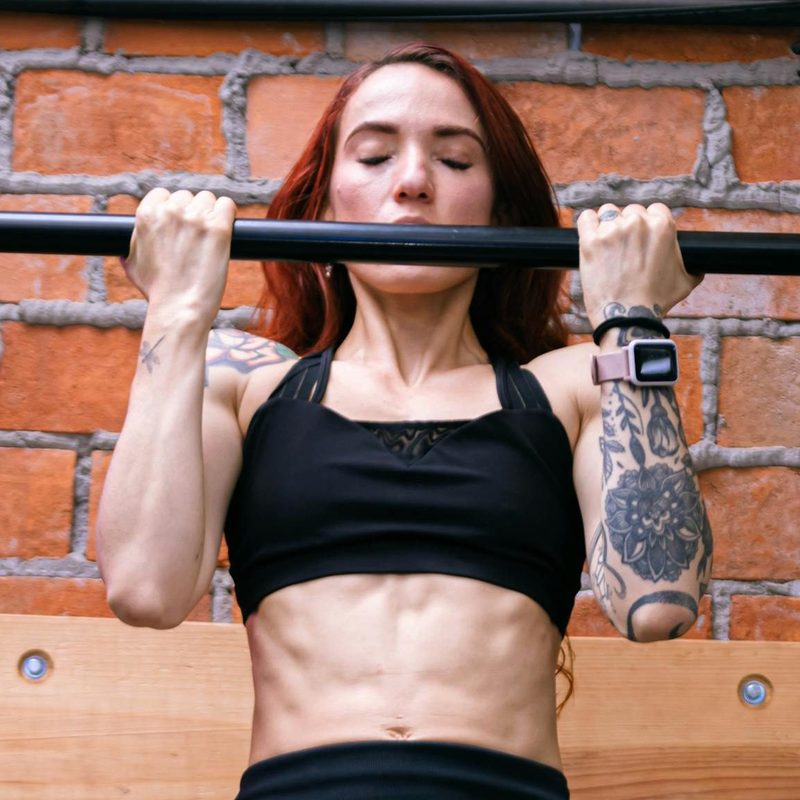 woman doing chin up wearing gym clothes near a brick wall