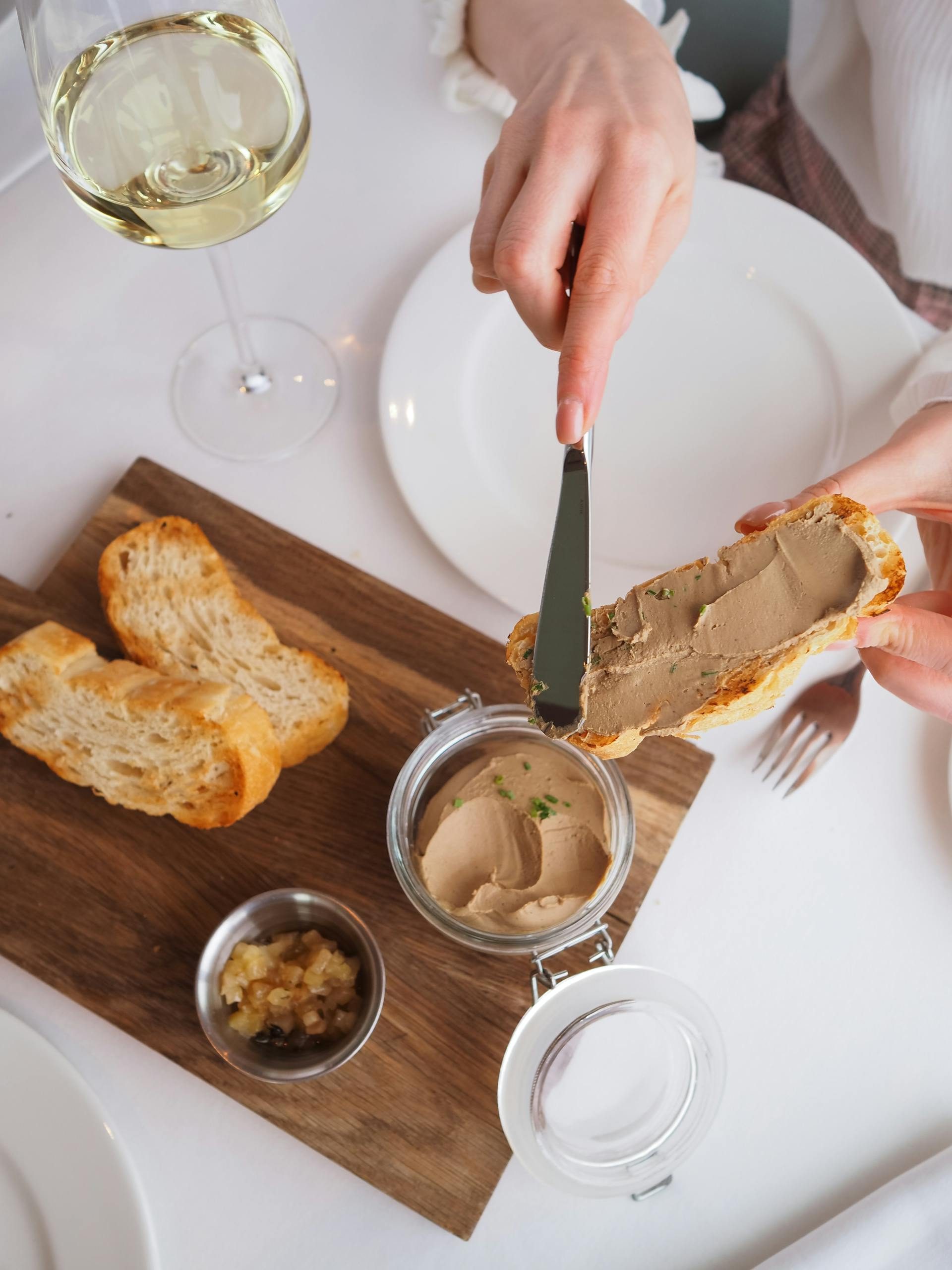 woman using cutting board spreading liver pate paste on bread on wooden board on table with white wine