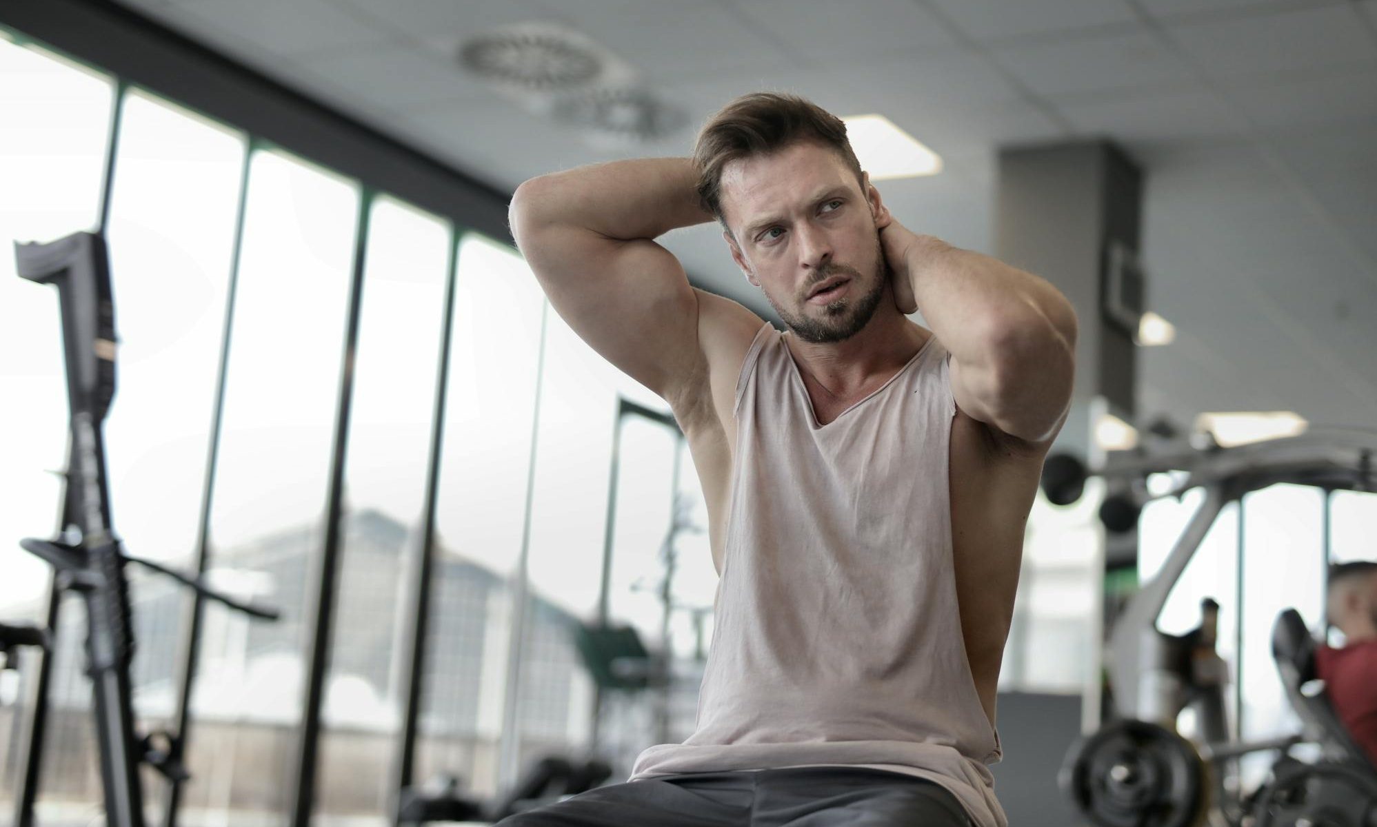 man sitting in gym wearing vest or tank top flexing biceps
