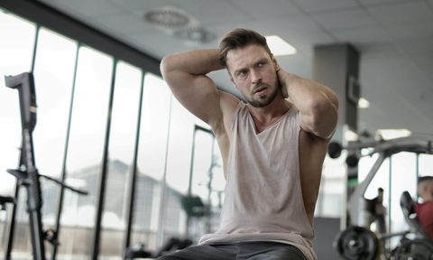 Man sitting in gym wearing vest or tank top flexing biceps bench tank