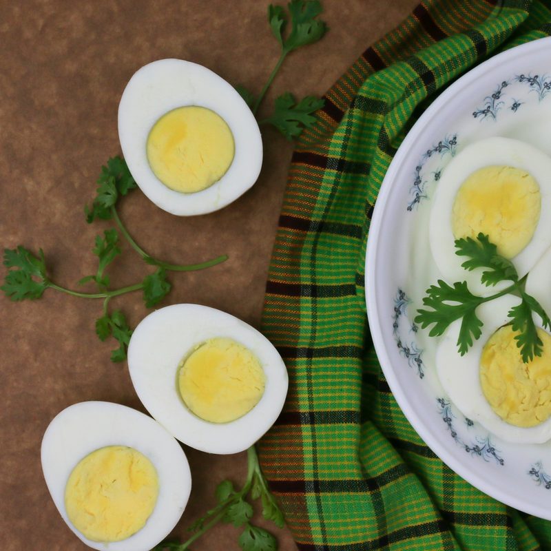 Hard-boiled eggs sliced open in half on brown countertop and white plate with green herbs
