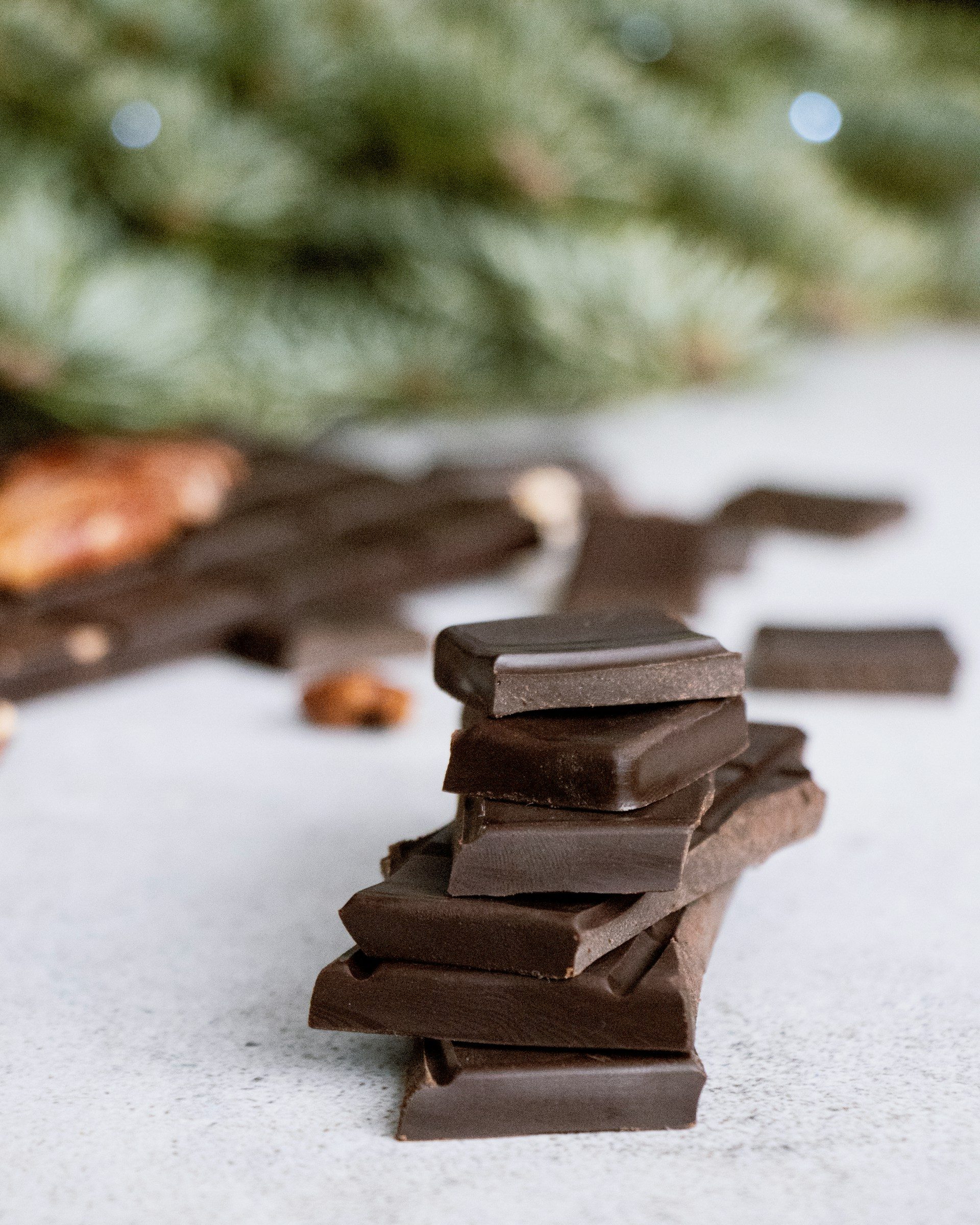 dark chocolate bar squares piled up on white counter top table with green tree in background