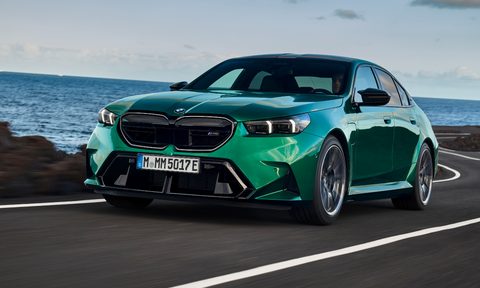 2025 BMW M5 performance sedan driving on a winding ocean-side paved road.