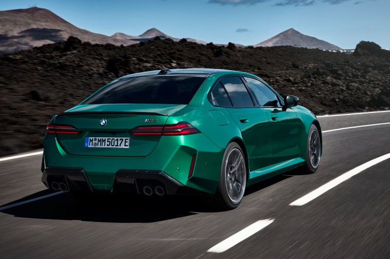 2025 BMW M5 performance sedan driving on a winding road with mountains in the background.