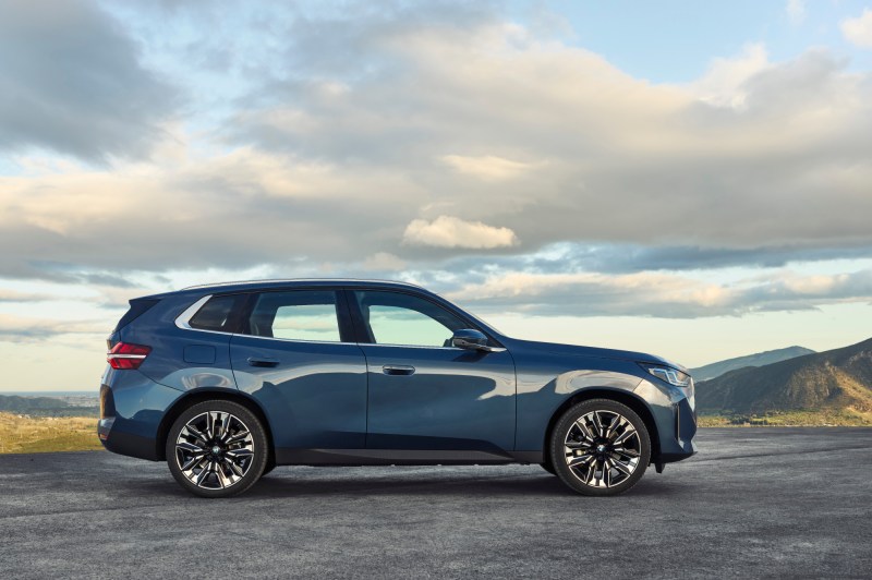 2025 BMW X3 30 xDrive right side profile view parked on dark gray gravel wih yellow grassy field and mountains in the backgroud.