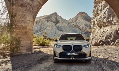 2025 BMW X3 M50 xDrive direct front view with the car parked under a stone structure in the desert.
