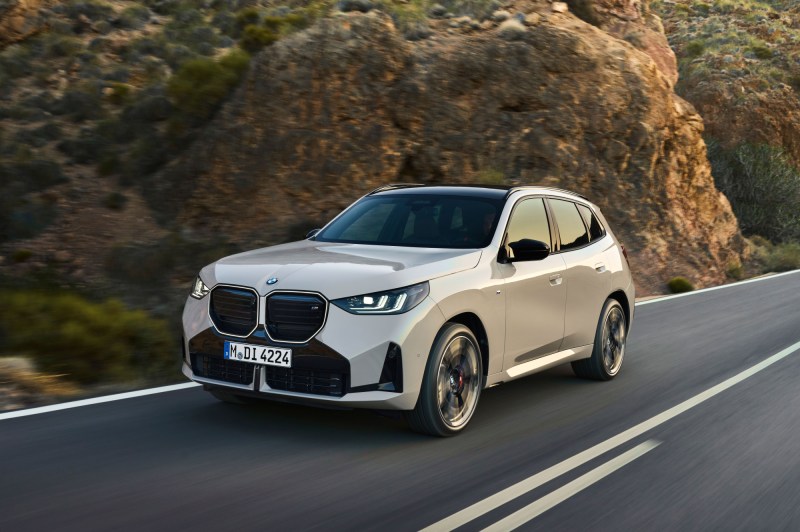2025 BMW X3 M50 xDrive left front three-quarter view driving on a road in the mountains.