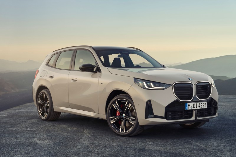 2025 BMW X3 M50 xDrive parked on top of a hill with hills and mountains in the background.