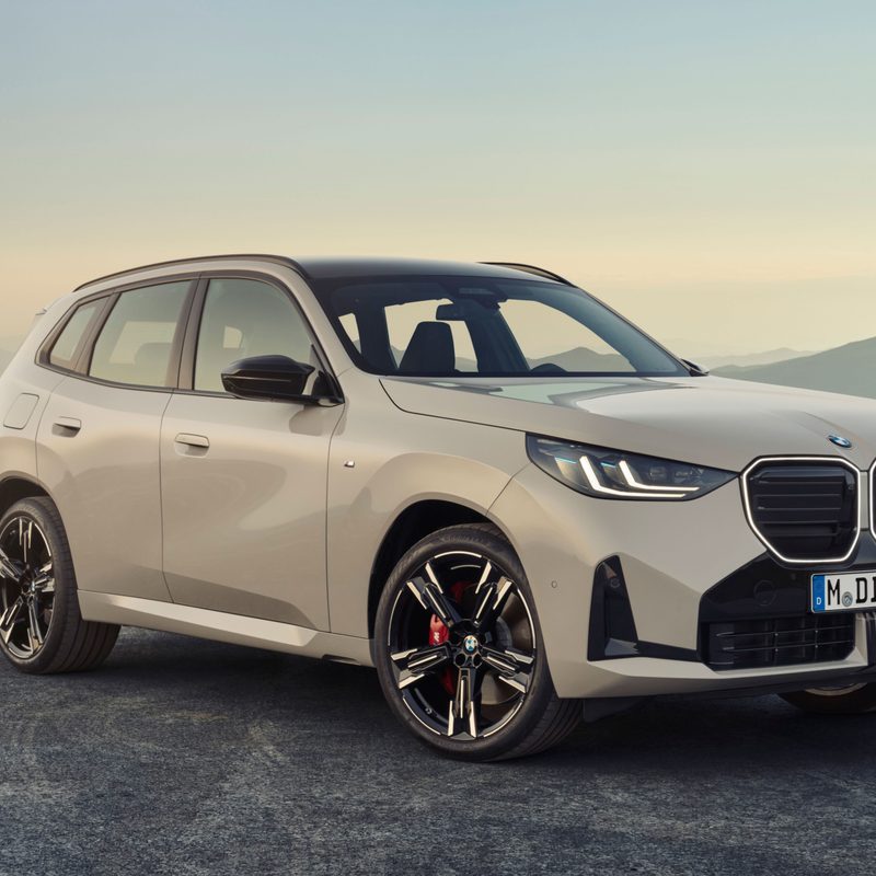 2025 BMW X3 M50 xDrive parked on top of a hill with hills and mountains in the background.