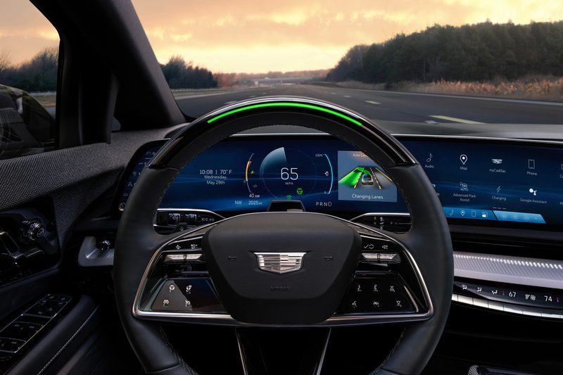 2025 Cadillac Optiq interior view of driver cickpit and dashboard driving on a highway with distant sunrise.