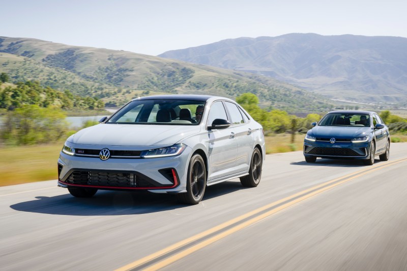 2025 VW Jetta GLI and 2025 VW Jetta left front three-quarter image driving on paved road with mountains in the background.