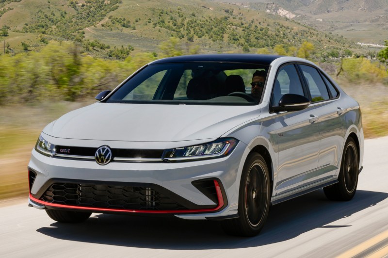 2025 VW Jetta GLI left front three-quarter view driving on a paved road in the countryside with mountains in the background.