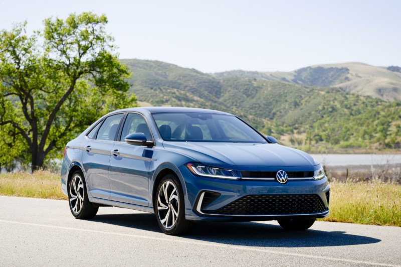 2025 VW Jetta right front three-quarter view driving on a paved road in the countryside with mountains in the background.