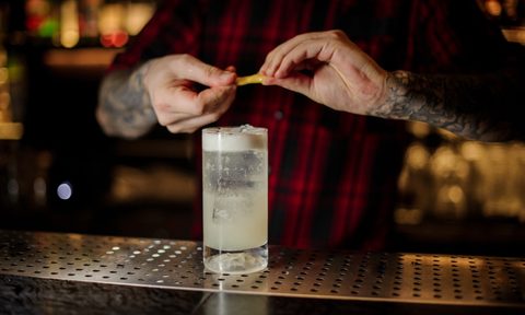 Bartender adding orange zest juice to a Gin Fizz cocktail in the glass on the bar counter