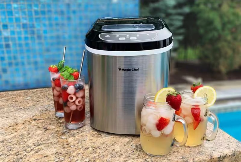 The Magic Chef 27-lbs Countertop Ice Maker next to iced drinks.