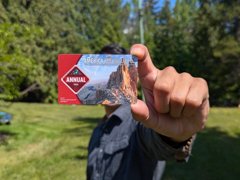 A man standing outdoors holding an America the Beautiful annual pass in front of his face