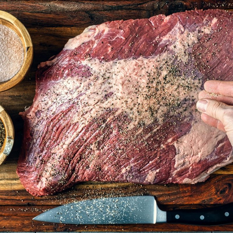 Seasoning a beef brisket with salt and pepper before barbequing on a smoker