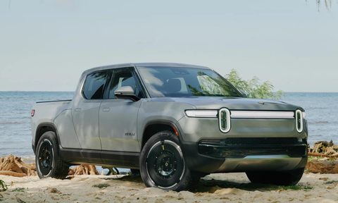 Second-generation Rivian R1T right front three-quarter view parked on a beach backed up to the rocks on the edge of the shore.