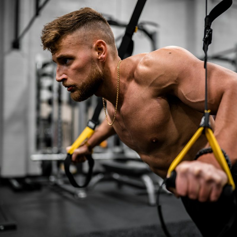 shirtless man with cable machine doing rear delt fly reverse fly with cable machine in gym-