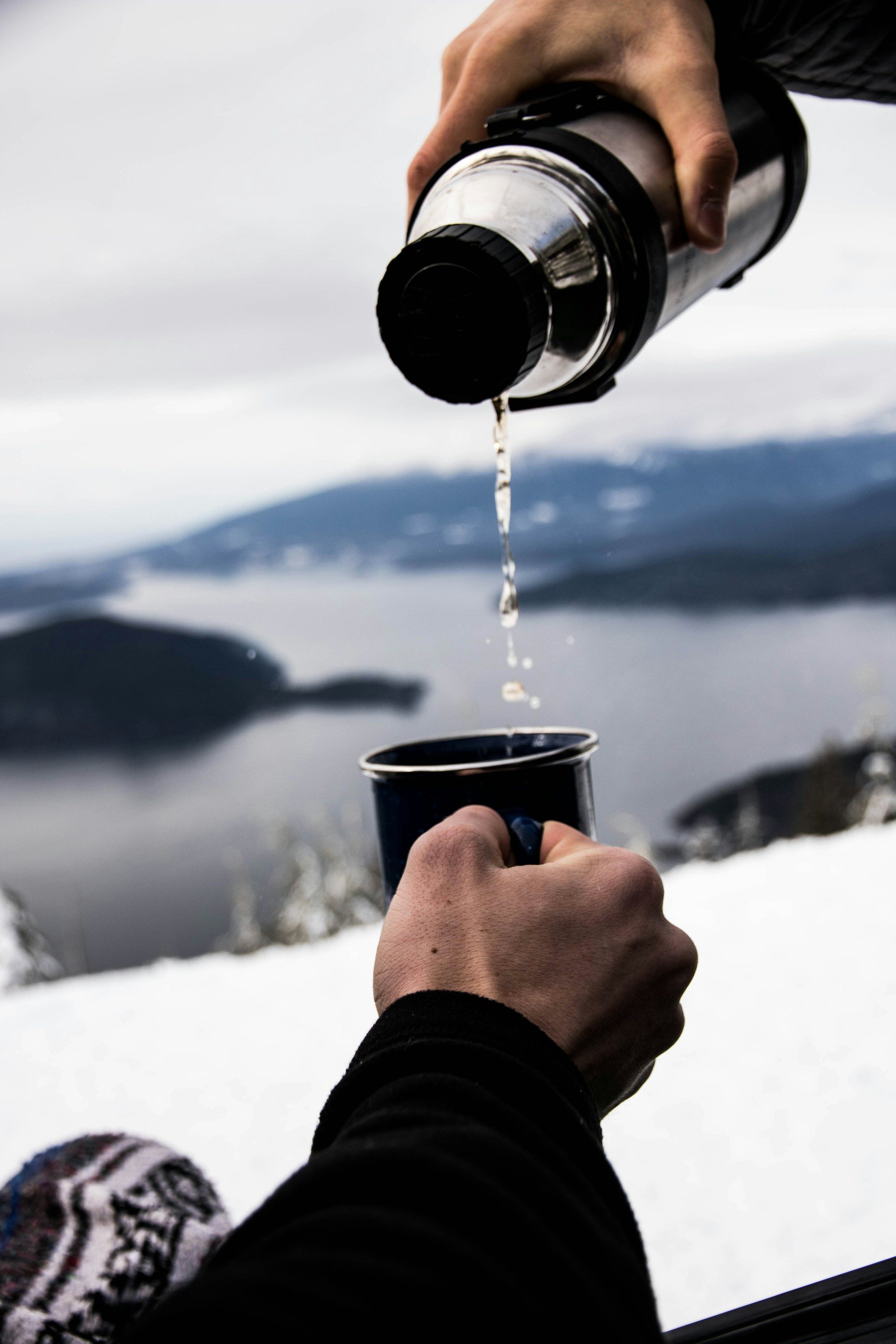 man hand pouring water from flask into black mug drinking hydration outside in nature water