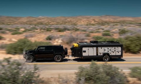 Exodus Capax travel trailer being towed by a black SUV down a desert highway.