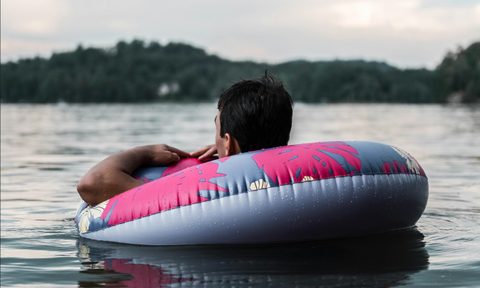 A man floating on a river in an inner tube on a cloudy day with hills in the background
