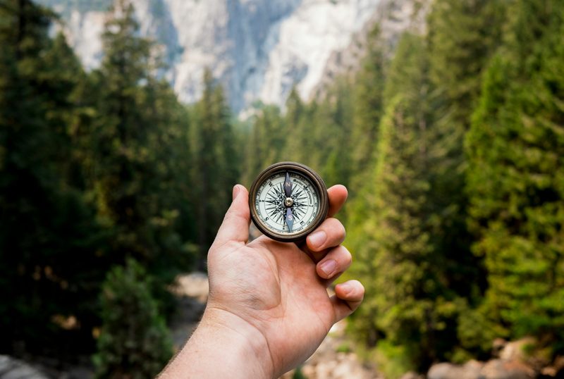 A man holding a compass in a natural area surrounded by trees