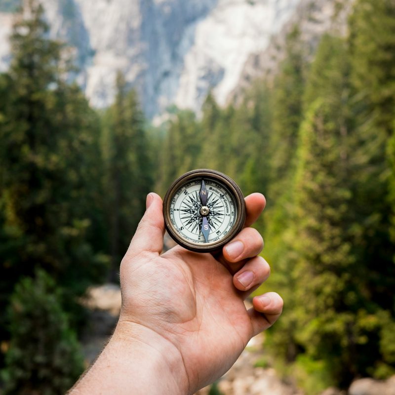 A man holding a compass in a natural area surrounded by trees