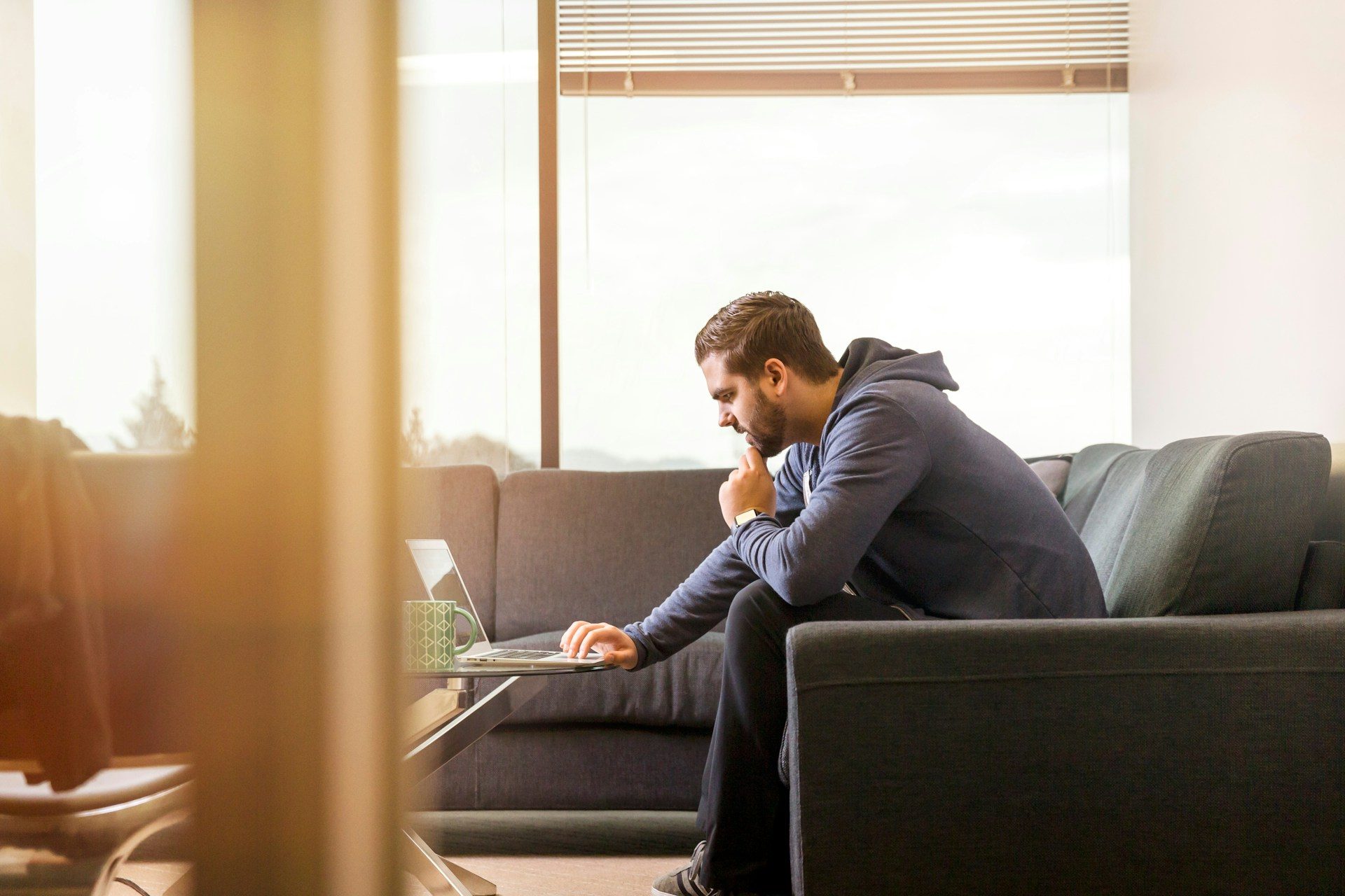 A man browsing his laptop sitting in a sunny living room