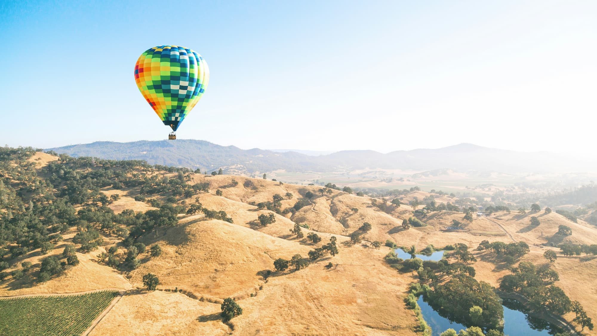 green and orange hot air balloon flying over mountains