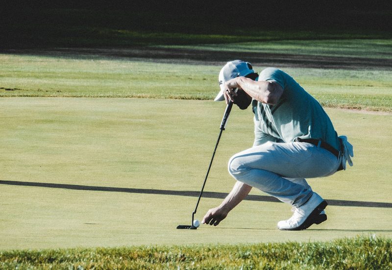 A person crouching to place the ball on a golf course.