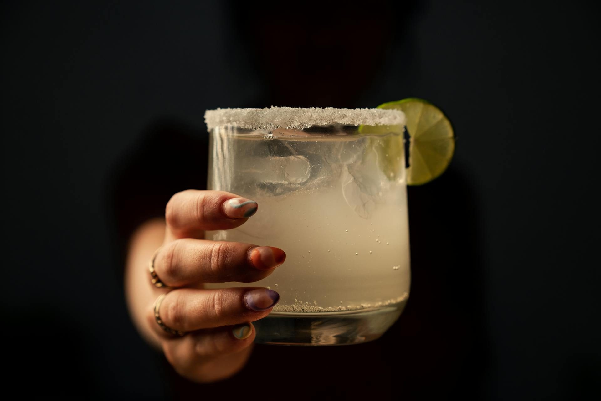 Person holding cocktail glass with salt on the rim and a lime wedge